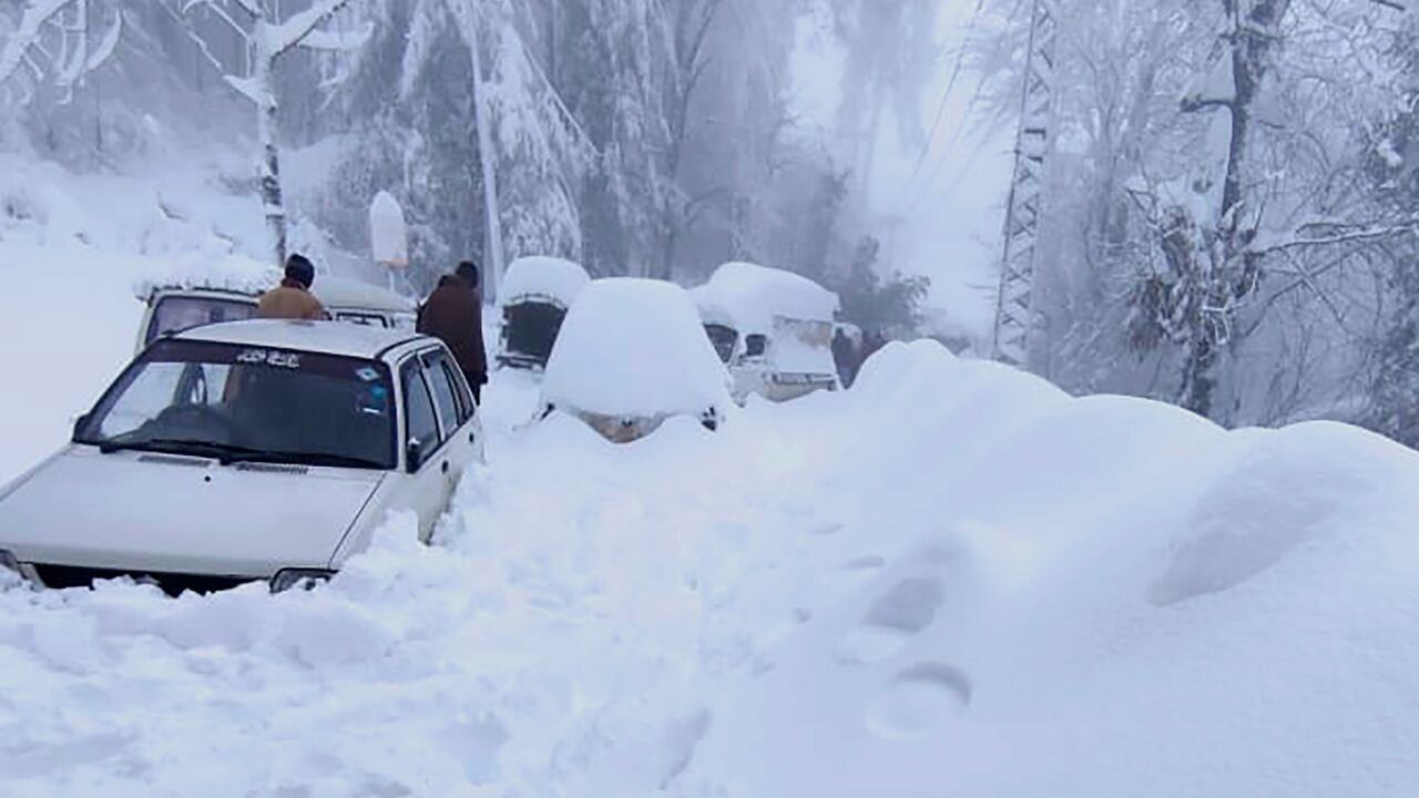 La gente pasa junto a vehículos atrapados en un área afectada por fuertes nevadas en Murree, a unos 45 kilómetros (28 millas) al norte de la capital de Islamabad, Pakistán.