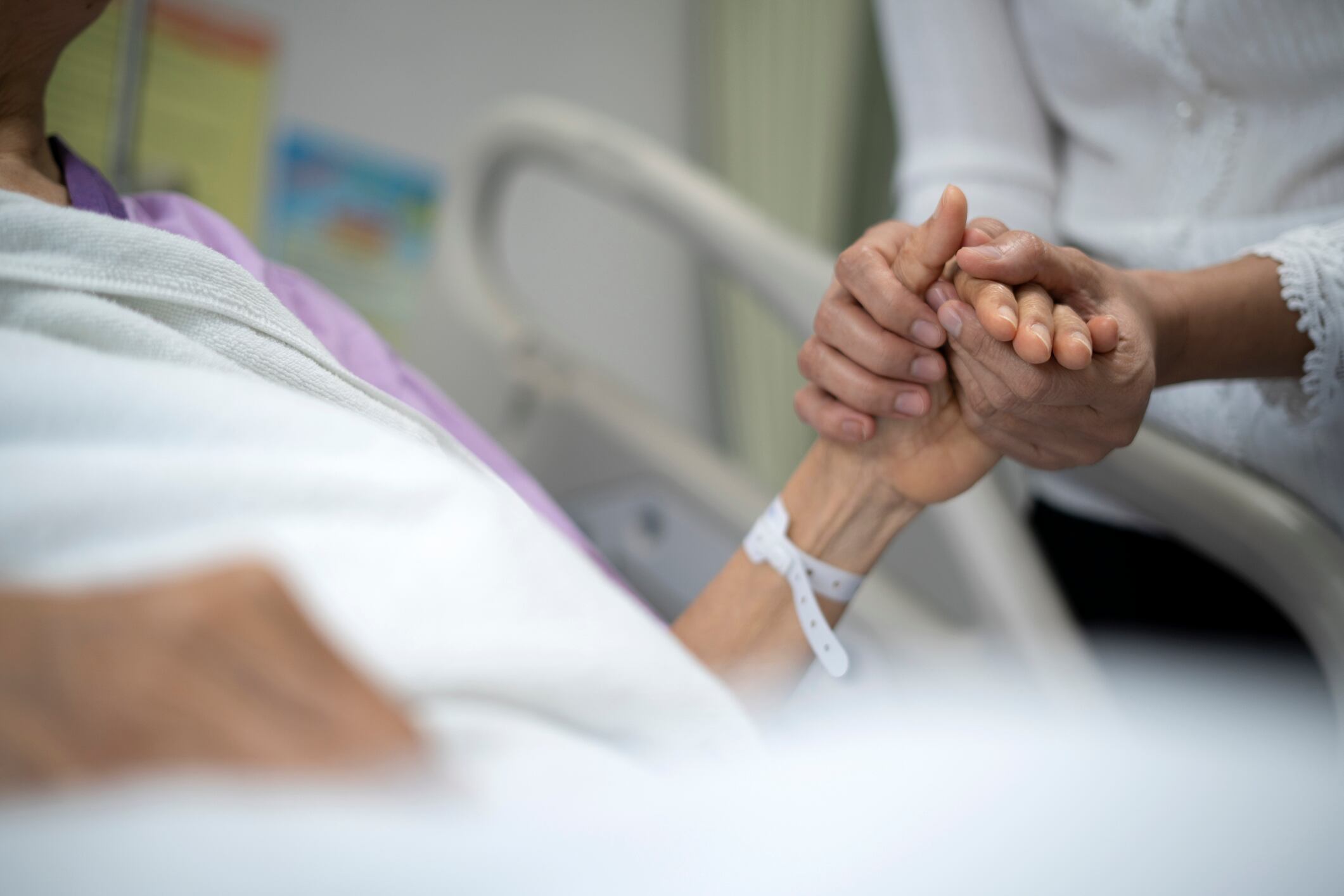 Foto de una hija sosteniendo la mano de su madre en la cama de un hospital