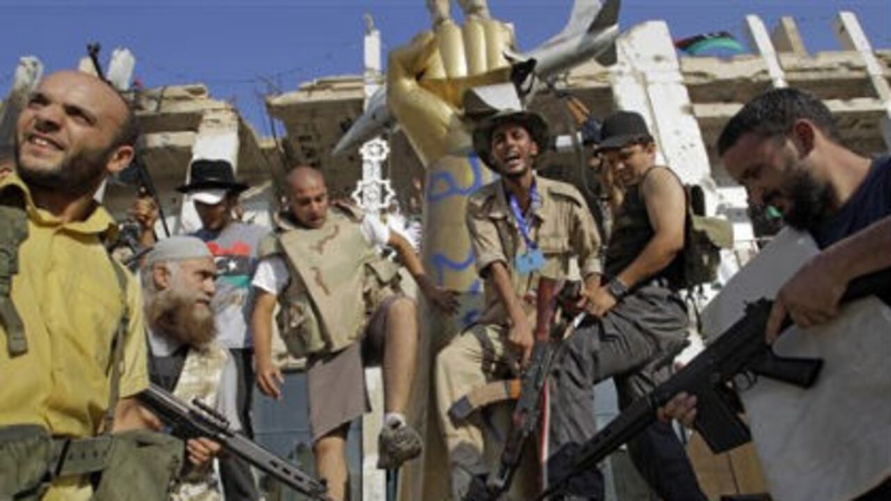 Rebeldes libios posan sobre la cabeza de una estatua del exlider libio Moammar Gadhafi, dentro del complejo de Bab Al-Aziziya, en Tripoli.