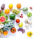 Vista superior de una bolsa de papel llena de varios tipos de frutas y verduras multicolores como papaya, tomates, manzanas rojas y verdes, zanahorias, champiñones, berenjenas, piña, cerezas, limón, ajo, naranjas y kiwi. La bolsa de papel está colocada en la esquina inferior izquierda sobre un fondo blanco y las frutas y verduras salen de ella.