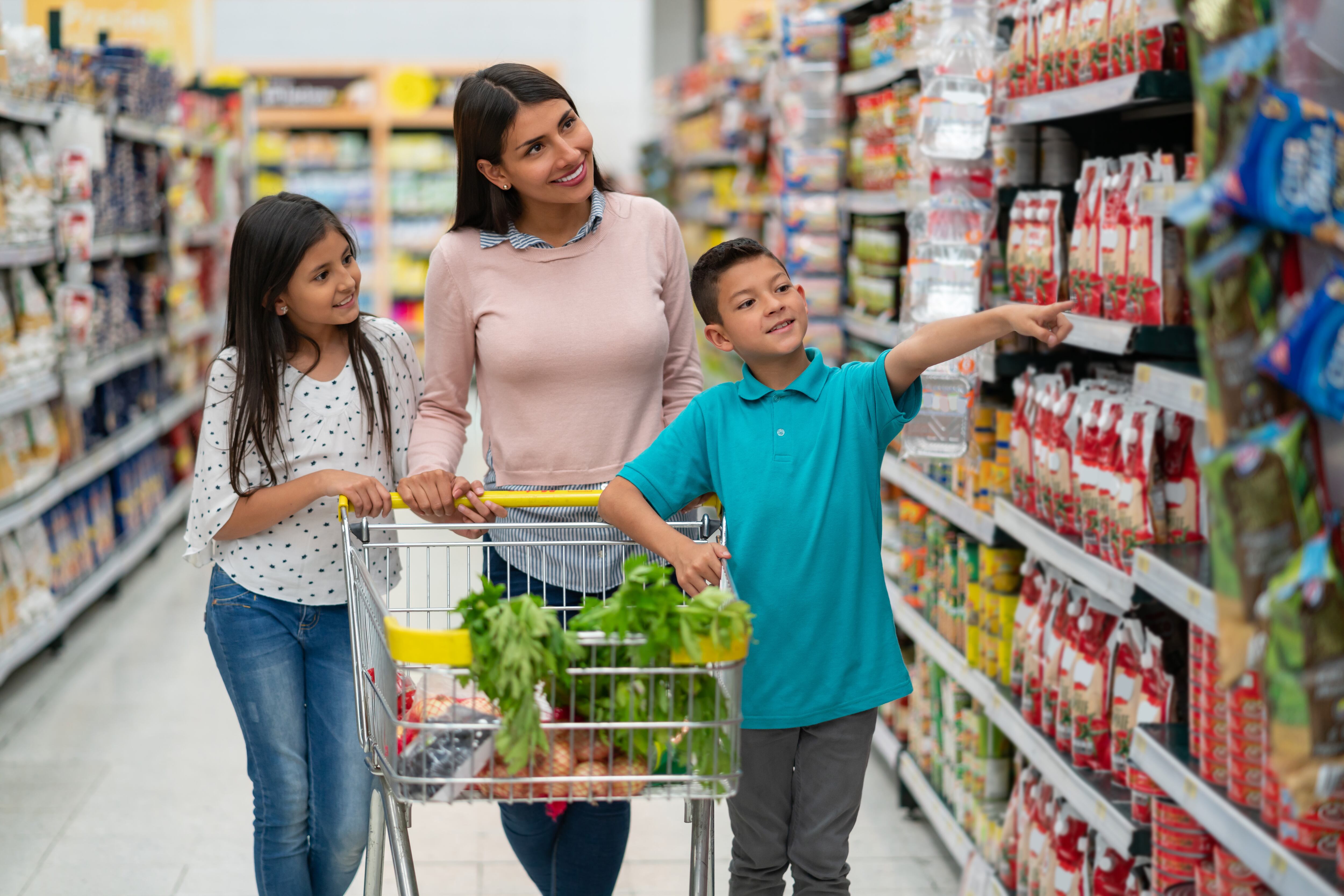 Beautiful latin american single parent with her two kids at the supermarket shopping for groceries and boy pointing at something both smiling