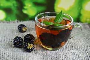 Blackberry tea with fresh picked blackberries in a glass cup on a burlap cloth background.Healthy drink,diet,alternative therapy or herbal medicine concept.