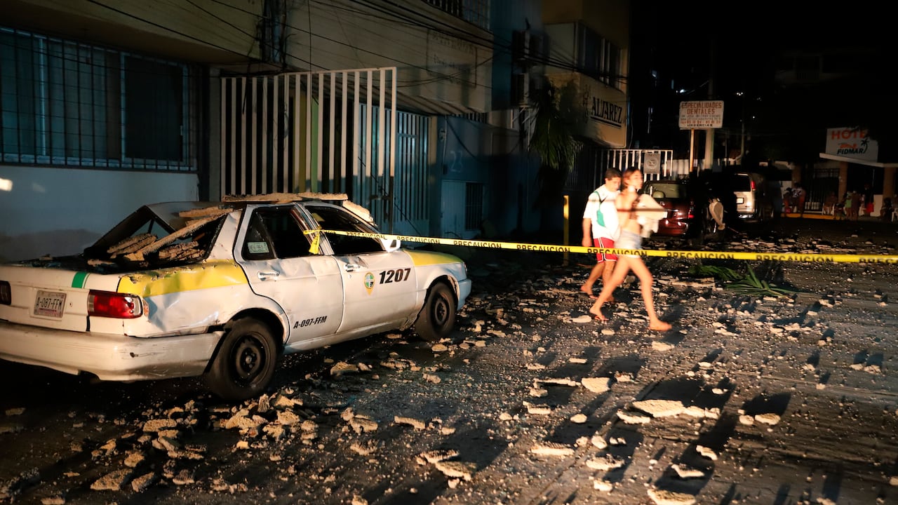 Una pareja pasa junto a un taxi que resultó dañado por la caída de escombros después de un fuerte terremoto en Acapulco, México, el martes, sept. 7 de febrero de 2021. (AP Photo/ Bernardino Hernandez)