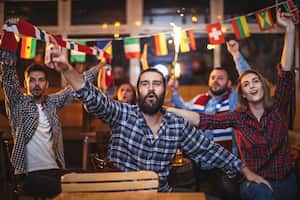 Group of young people, sitting in a pub all together, watching a sports game.