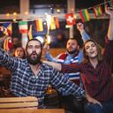 Group of young people, sitting in a pub all together, watching a sports game.