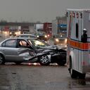 Car crash on major highway during rainfall at night. Ambulance in foreground and police car in background.
