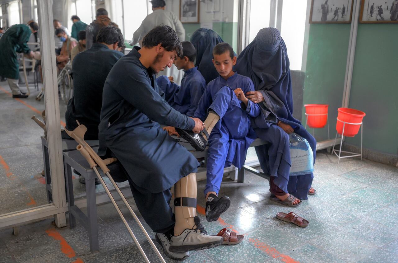 In this photograph taken on October 11, 2021, a man helps a boy put on shoes on his new prosthetic leg at the International Committee of Red Cross Rehabilitation Centre in Kabul. - Just months ago they were fighting each other as mortal enemies, but today they are amputees dealing with their new disability, together. At this Red Cross-run rehabilitation centre in Kabul, former Afghan government soldiers and Taliban fighters adjust their new prostheses, living side by side. (Photo by BULENT KILIC / AFP) / TO GO WITH: Afghanistan-conflict-health-disability, FOCUS by Emmanuel Peuchot