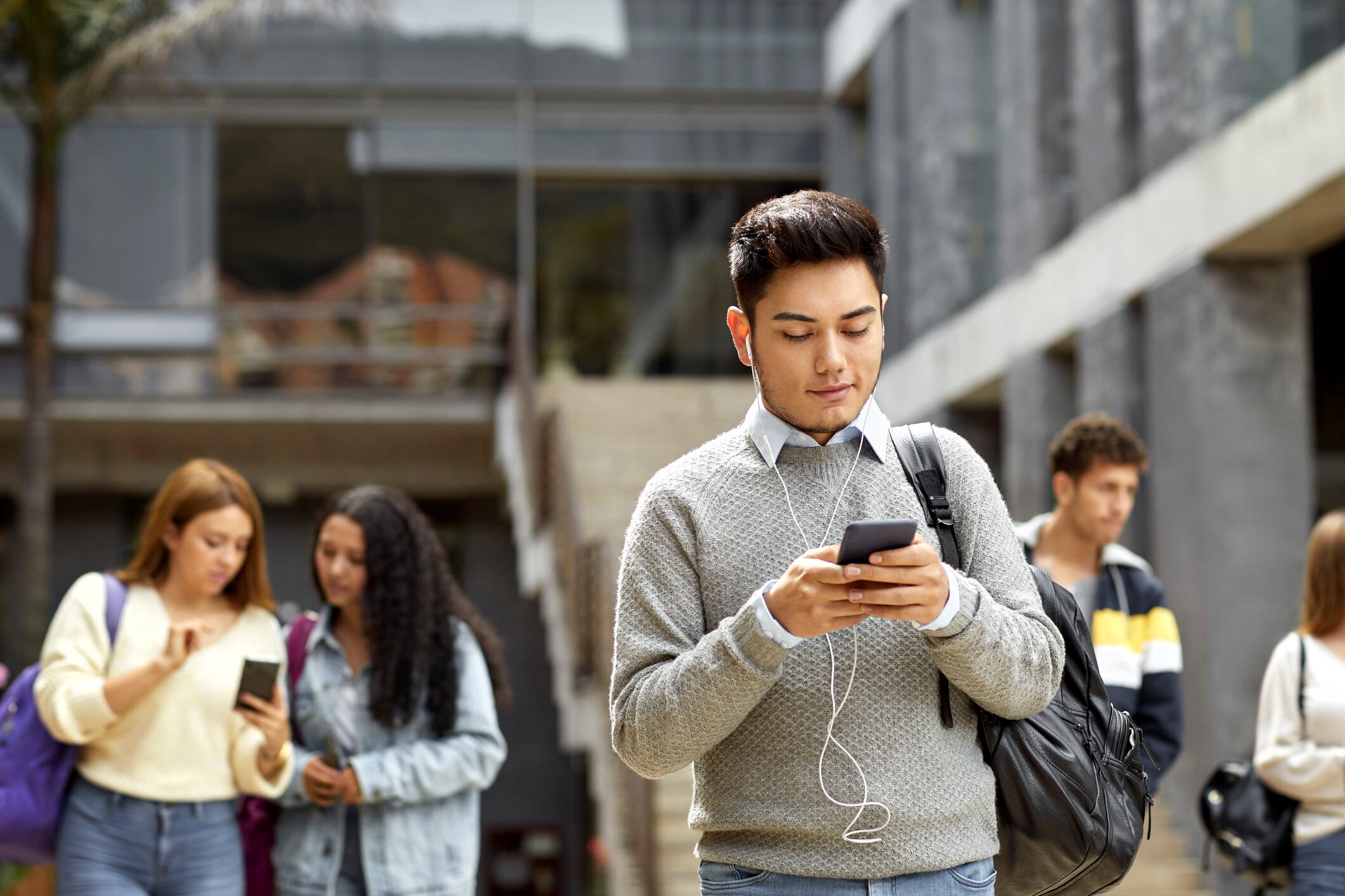 Male student texting from cell in campus. Young man listening to music at university. He is using smart phone.