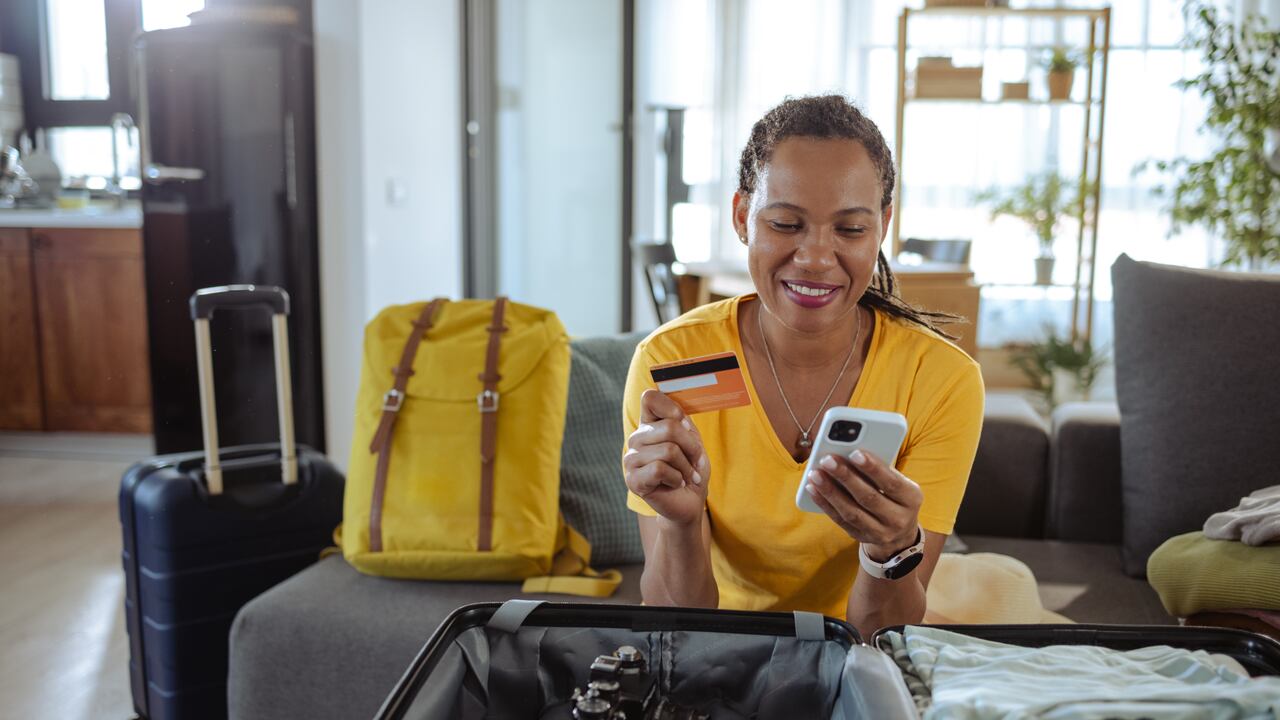 Mujer haciendo la maleta para un viaje y reservando en línea a través de su celular.