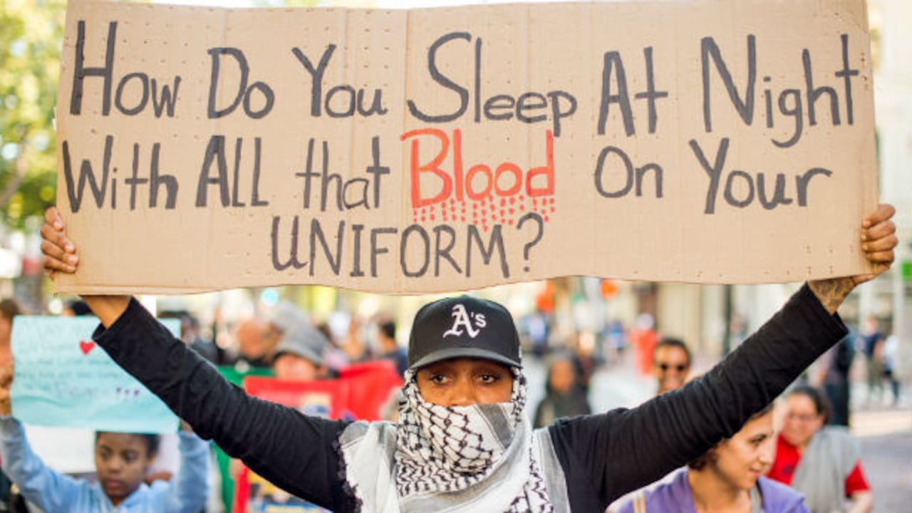 Una mujer sostiene un cartel que dice: "¿Cómo duermen de noche con toda esa sangre en su uniforme?", durante una protesta de cientos de manifestantes en Oakland, California (EE. UU.), el 20 de agosto, 2014.