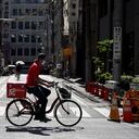 Un repartidor que lleva una máscara protectora para ayudar a frenar la propagación del coronavirus monta en bicicleta. Foto AP / Eugene Hoshiko