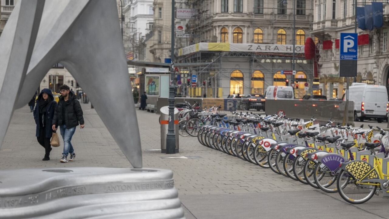 La gente pasa junto a las bicicletas de alquiler en las afueras de la Ópera Estatal, en el centro de la ciudad de Viena, que normalmente está llena de gente, en Viena, Austria, el 22 de noviembre de 2021 (Photo by JOE KLAMAR / AFP)