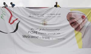 Municipality workers install posters welcoming Pope Francis in the Iraqi capital Baghdad, on March 4, 2021, on the eve of the pontiff's first visit to Iraq. - Pope Francis begins his historic trip to war-scarred Iraq on March 5, defying security concerns and the coronavirus pandemic to comfort one of the world's oldest and most persecuted Christian communities. (Photo by AHMAD AL-RUBAYE / AFP)