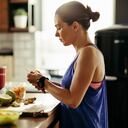 Young sportswoman making herself a healthy smoothie and slicing fresh fruit in the kitchen.
