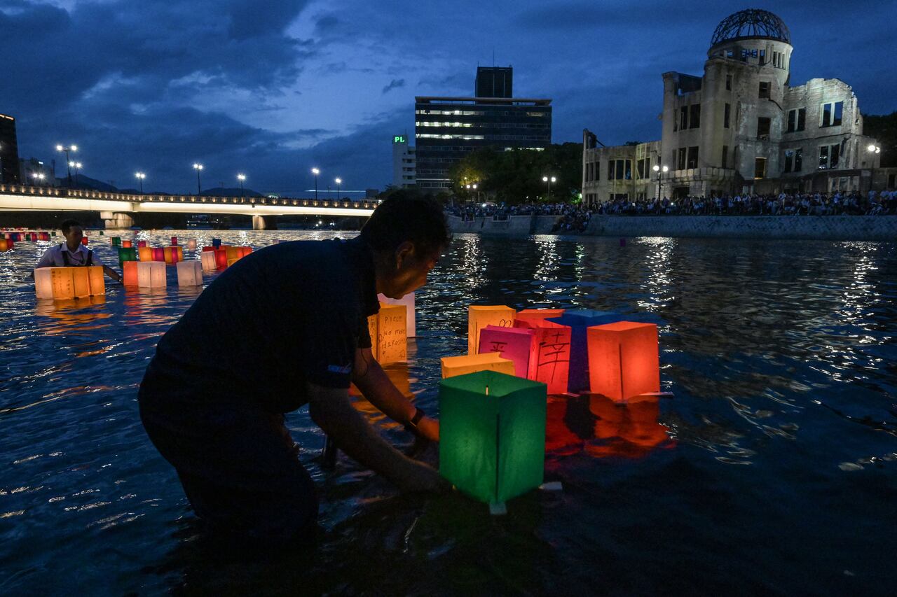 Voluntarios (izq.) empujan linternas de papel hacia el río Motoyasu, pasando por la cúpula de la bomba atómica (detrás), después de que fueron liberadas por visitantes para conmemorar el 80.º aniversario del primer ataque con bomba atómica del mundo, en la ciudad de Hiroshima el 6 de agosto de 2025. (Foto de Richard A. Brooks / AFP)