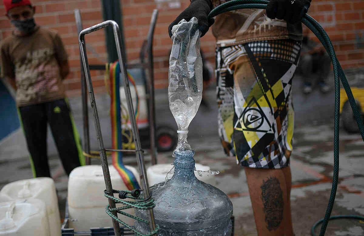 Un hombre llena su tanque de agua valiéndose de una botella plástica y una manguera en el barrio de Esperanza de Caracas, Venezuela, el domingo 7 de junio de 2020. Foto: Matias Delacroix / AP.