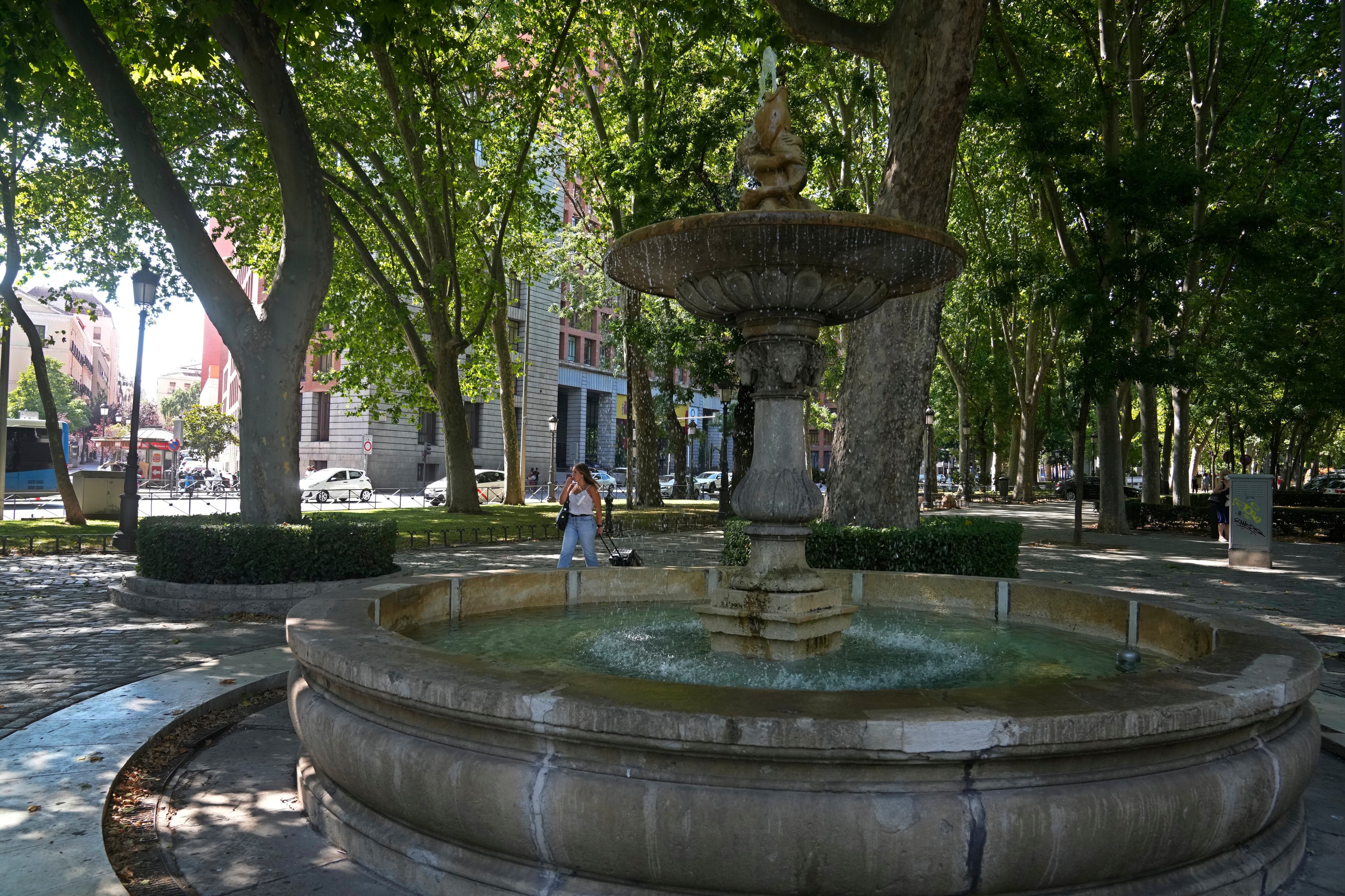 Una mujer camina junto a una fuente en el Paseo del Prado en Madrid, España, el viernes 23 de julio de 2021. El arbolado Paseo del Prado de Madrid y el parque del Retiro adyacente han sido incluidos en la lista del Patrimonio Mundial de la UNESCO. El Comité del Patrimonio Mundial de la UNESCO respaldó la candidatura que destaca la introducción de la naturaleza en la capital española. (AP Photo/Paul White)