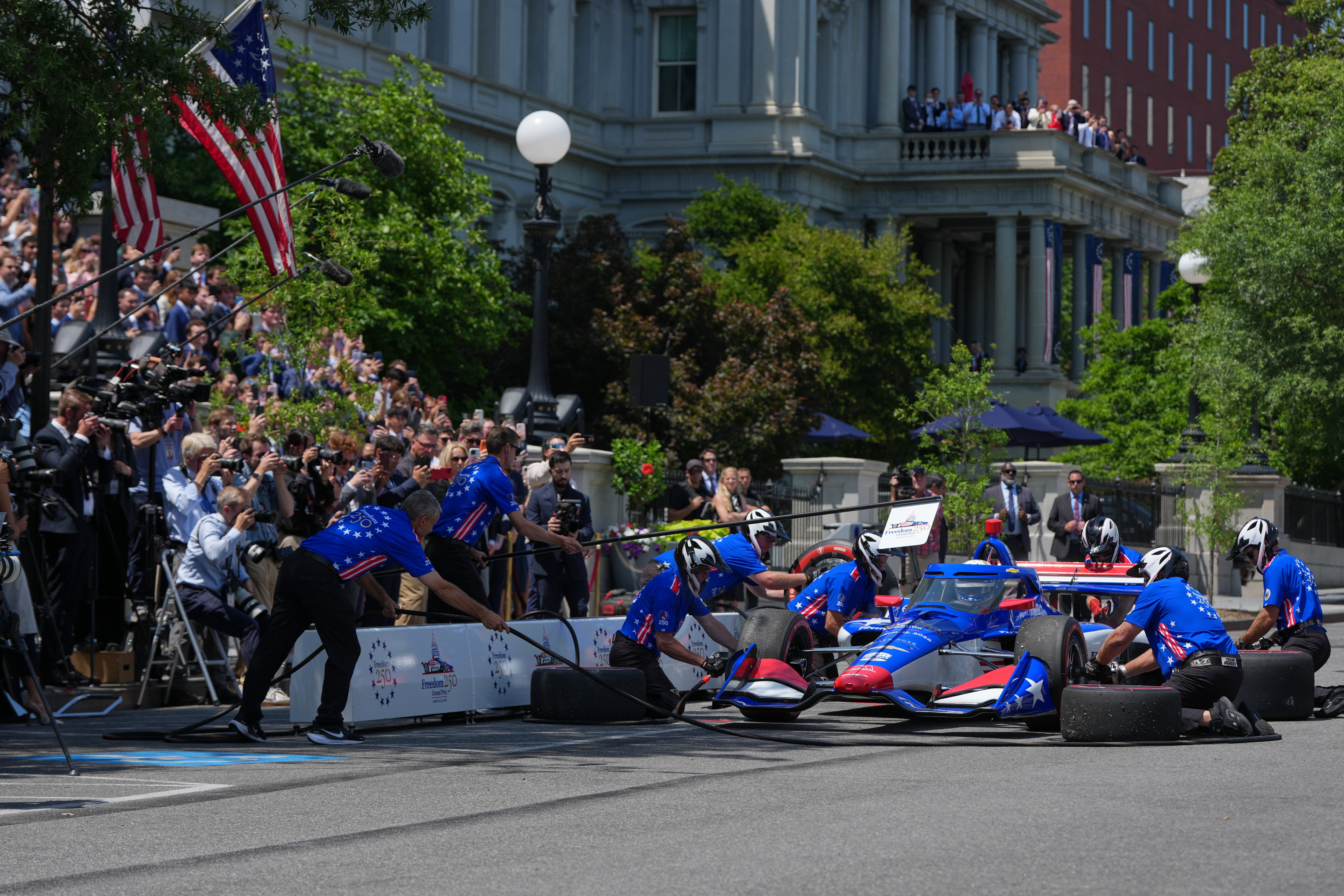 Un equipo de mecánicos cambia los neumáticos de un vehículo de carreras pilotado por David Malukas, de la IndyCar Series, durante un evento en West Executive Drive —junto al presidente Donald Trump— en la Casa Blanca, para promocionar la próxima carrera automovilística Freedom 250 Grand Prix, el lunes 13 de julio de 2026, en Washington. (Foto AP/Julia Demaree Nikhinson)