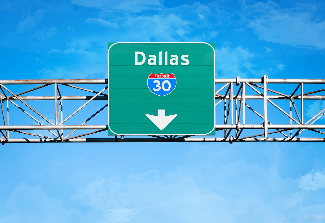 An elevated overhead highway sign. It reads "Dallas" and has an Interstate 30 shield above an arrow pointing downward.