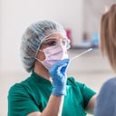 Well-protected medical staff performs swab test for Covid-19 to a young blonde female patient.