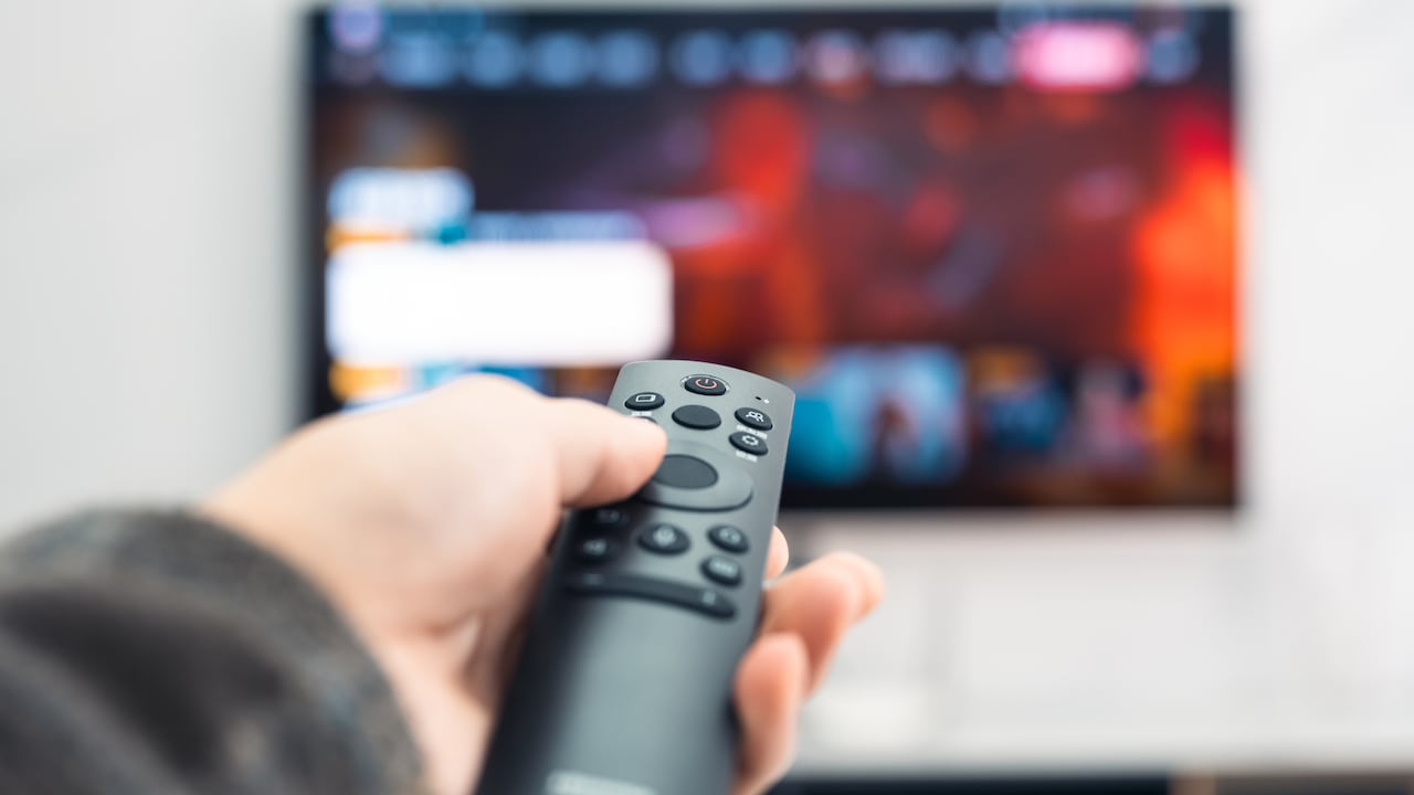 Close-up of a man holding a TV remote control in his hand. Express the concept of watching smart audiovisual devices at home.