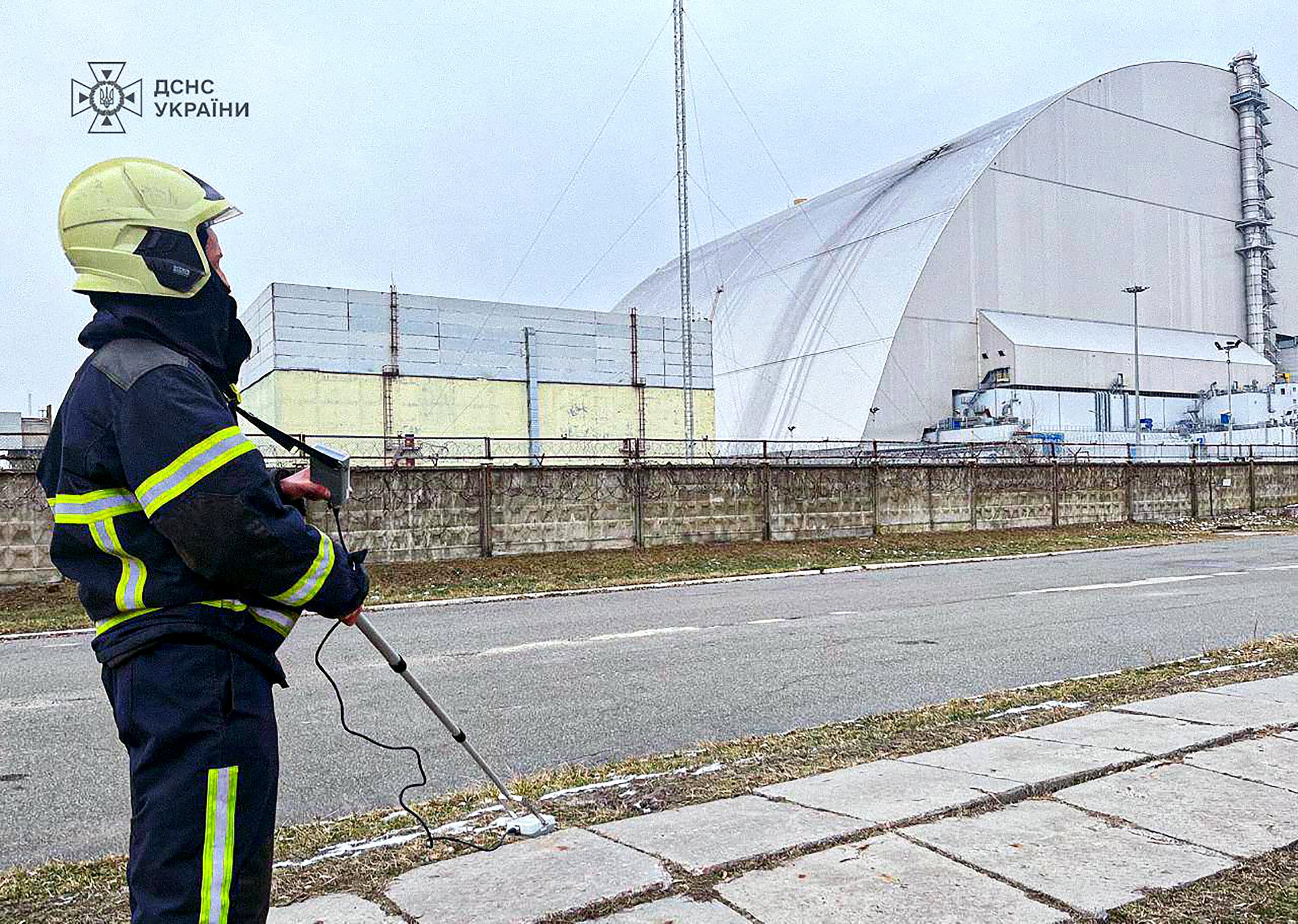 This handout photograph taken and released by Ukrainian Emergency Service on February 14, 2025 shows an employee working outside the New Safe Confinement (NSC), which protects the remains of reactor 4 of the former Chernobyl Nuclear Power Plant following a drone attack on its cover built to contain radiation. Ukraine's president said on February 14, that a Russian drone had struck overnight a cover built to contain radiation at the Chernobyl nuclear power plant. (Photo by Handout / UKRAINIAN EMERGENCY SERVICE / AFP) / RESTRICTED TO EDITORIAL USE - MANDATORY CREDIT "AFP PHOTO /  UKRAINIAN EMERGENCY SERVICE " - NO MARKETING NO ADVERTISING CAMPAIGNS - DISTRIBUTED AS A SERVICE TO CLIENTS
