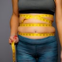 Mujer en ropa activa con cinta métrica exprimida sobre un fondo gris Mujer en ropa activa con cinta métrica exprimida sobre un fondo gris