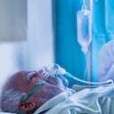 Preocupado miembro de la familia o médico con EPP o traje protector rezando por el coronavirus o el paciente infectado con covid-19 para recuperarse en el hospital mientras el paciente respira con una máscara de oxígeno del ventilador