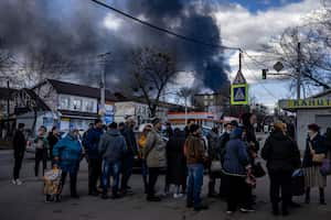La gente hace fila frente a un supermercado mientras el humo se eleva sobre la ciudad de Vasylkiv, en las afueras de Kiev, el 27 de febrero de 2022, después de que los ataques rusos durante la noche golpearan un depósito de petróleo. (Foto de Dimitar DILKOFF / AFP)