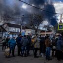 La gente hace fila frente a un supermercado mientras el humo se eleva sobre la ciudad de Vasylkiv, en las afueras de Kiev, el 27 de febrero de 2022, después de que los ataques rusos durante la noche golpearan un depósito de petróleo. (Foto de Dimitar DILKOFF / AFP)