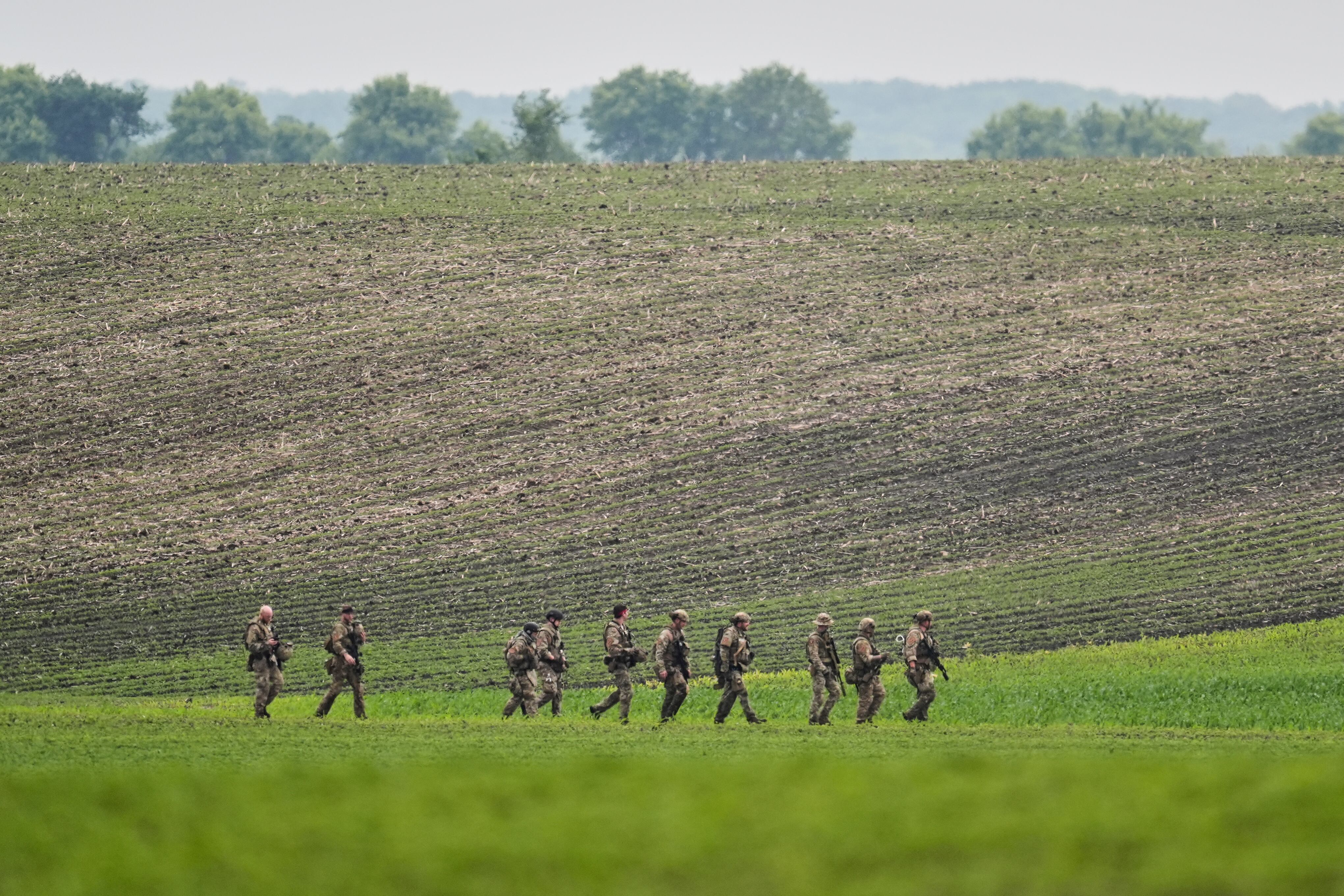 Members of law enforcement agencies walk through a field near a vehicle suspected to belong to shooting suspect, Vance Boelter, Sunday, June 15, 2025, in Belle Plaine, Minn. (AP Photo/George Walker IV)