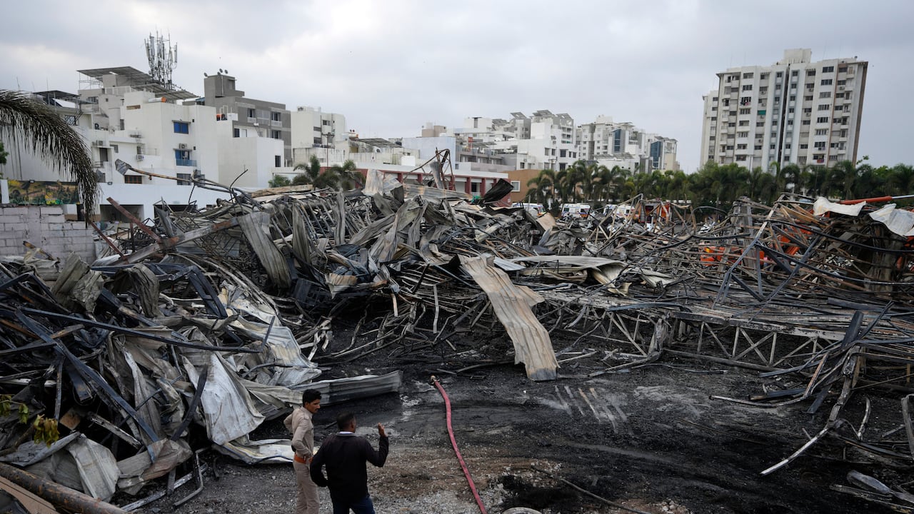 Los bomberos se encuentran junto a escombros quemados el día después de que se produjera un incendio en un parque de diversiones en Rajkot, India, el domingo 26 de mayo de 2024. Un incendio masivo dañó gran parte del parque el sábado, matando a más de veinte personas e hiriendo a algunas. otros, dijeron informes de prensa.