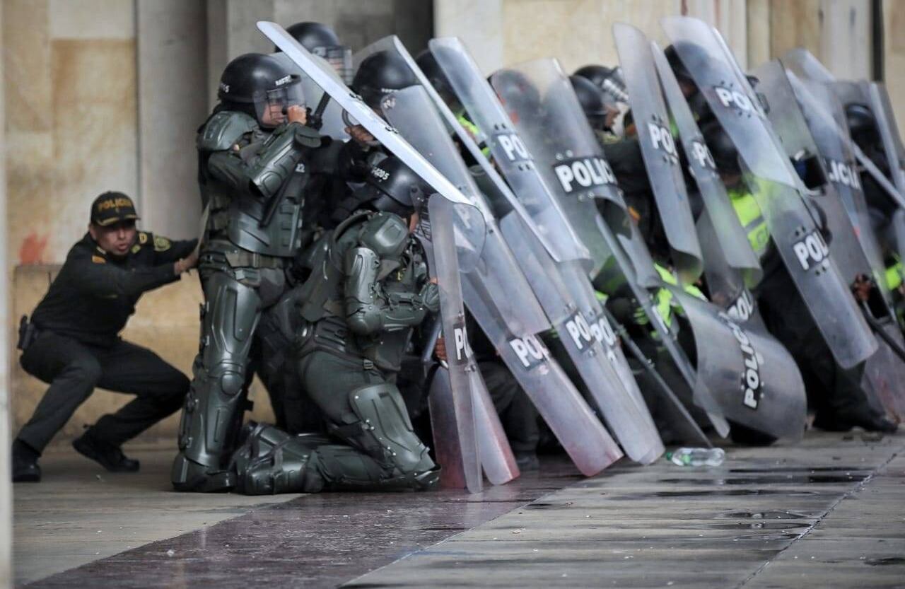 Un uniformado se escuda en sus compañeros para no ser víctima de los ataque a piedra y ladrillo.