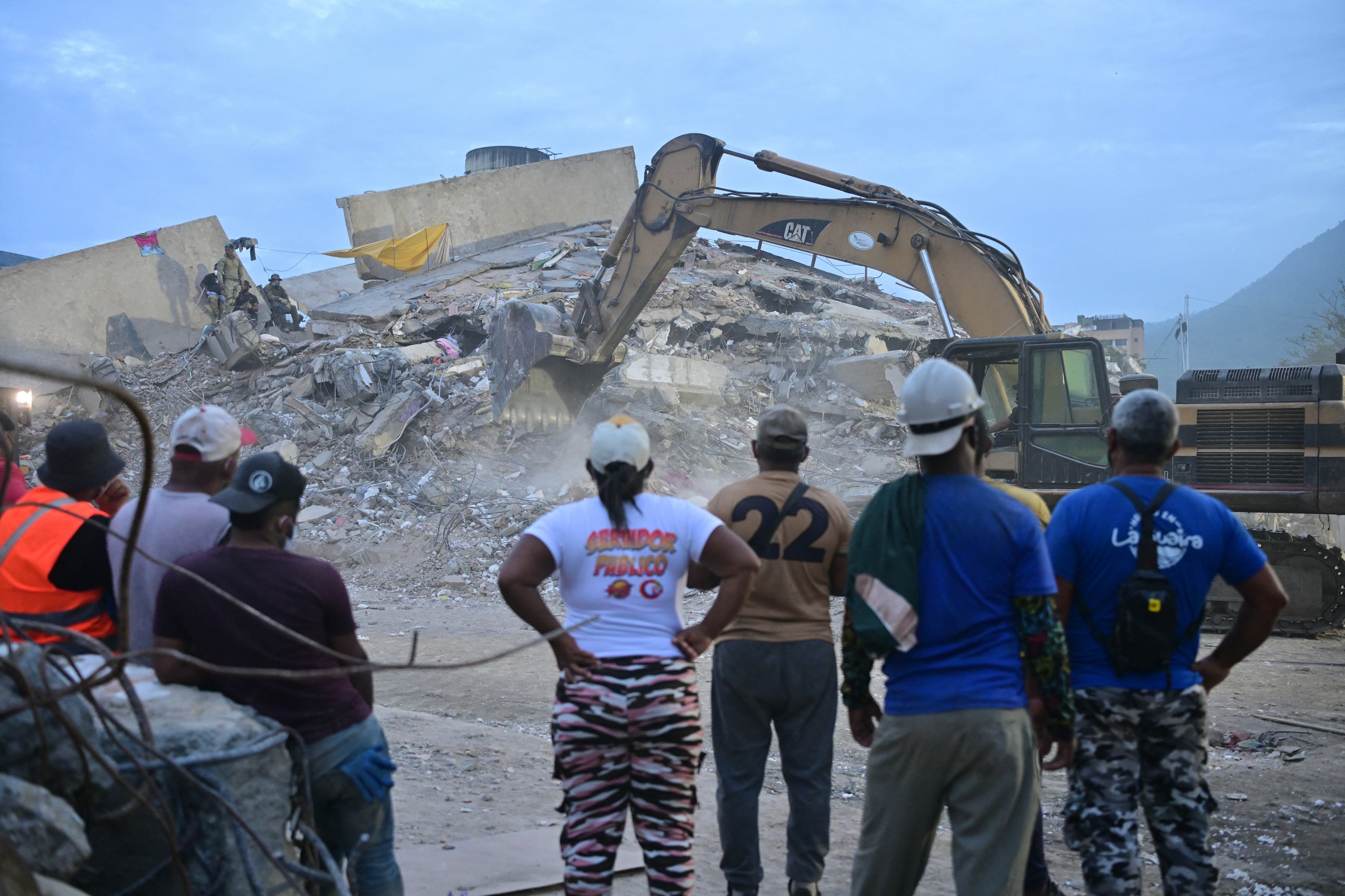 Voluntarios y residentes observan cómo una excavadora retira escombros de un edificio derrumbado en Caraballeda, estado de La Guaira, Venezuela, el 3 de julio de 2026