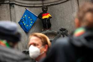 Personas, con tapabocas para prevenir la propagación del coronavirus, toman fotografías del hito del Manneken Pis vestido con los colores de la bandera alemana junto a una bandera de la UE en el centro de Bruselas. Foto: AP / Francisco Seco