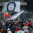 SANTIAGO, CHILE - JANUARY 03: Demonstrator carry a flag with face of popular singer Victor Jara whle a watter cannon fires against them during the first protest of the year against Chilean government on January 3, 2020 in Santiago, Chile. Chile's senate has announced today they will approve an increase of taxes on the richest individuals of the country as Chile's economy contracted 3.3% in November. Protests and social unrest arose on October 18 after a subway fare increase which developed in a social movement demanding improvements in basic services, fair prices and benefits including pensions, public health and education. (Photo by Marcelo Hernandez/Getty Images)