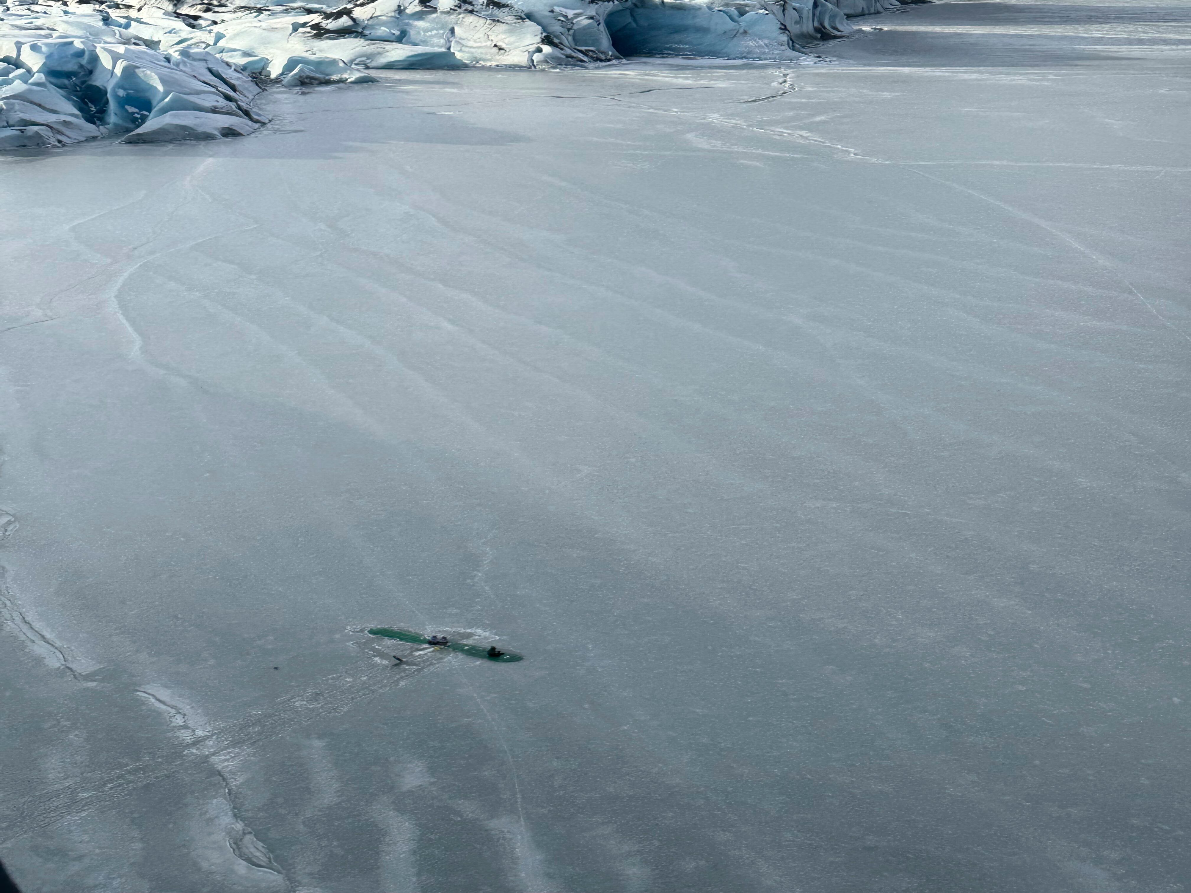 This photo provided Monday, March 24, 2025 by Dale Eicher shows an airplane partially submerged into the ice of Tustumena Lake near Soldotna, Alaska, with the three survivors standing on the plane's wing. (Dale Eicher via AP)