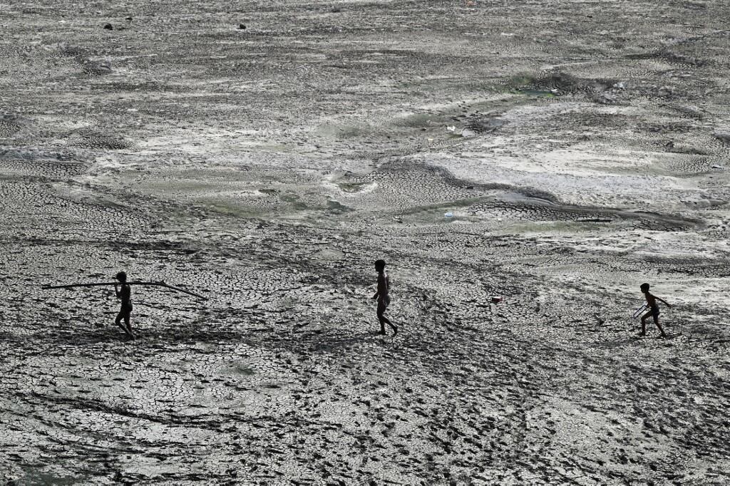 La gente camina por un tramo del lecho reseco del río Yamuna en un caluroso día de verano en Nueva Delhi el 2 de mayo de 2022. (Foto de Sajjad HUSSAIN / AFP)
