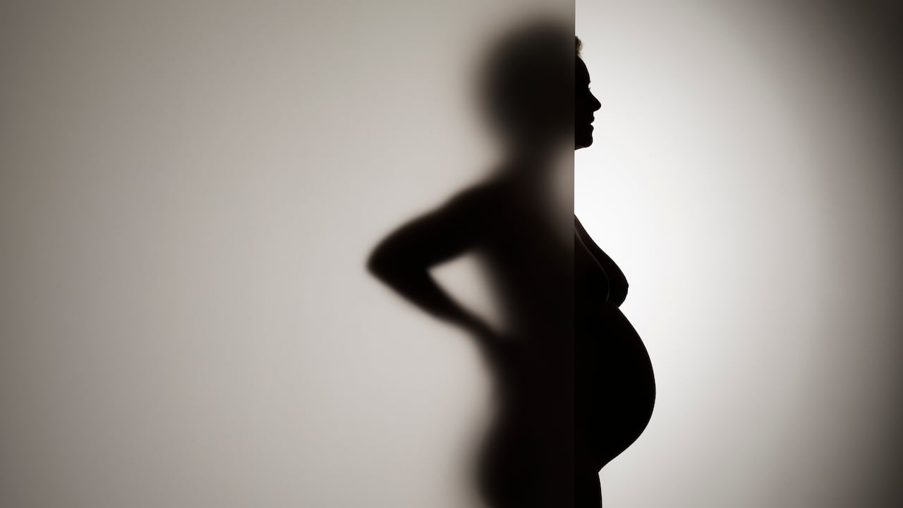 Heavily pregnant woman half standing blocked behind frosty glass with her bump protruding