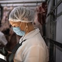 Carnicero femenino con tableta digital con mascarilla en cámara frigorífica