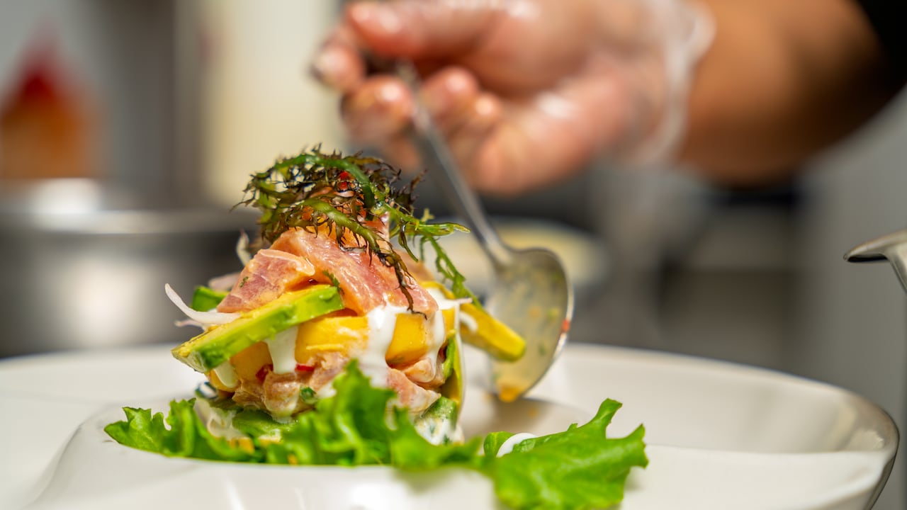 Chef añadiendo el toque final a una colorida ensalada peruana de mariscos, con mango fresco, aguacate y una salsa cremosa.