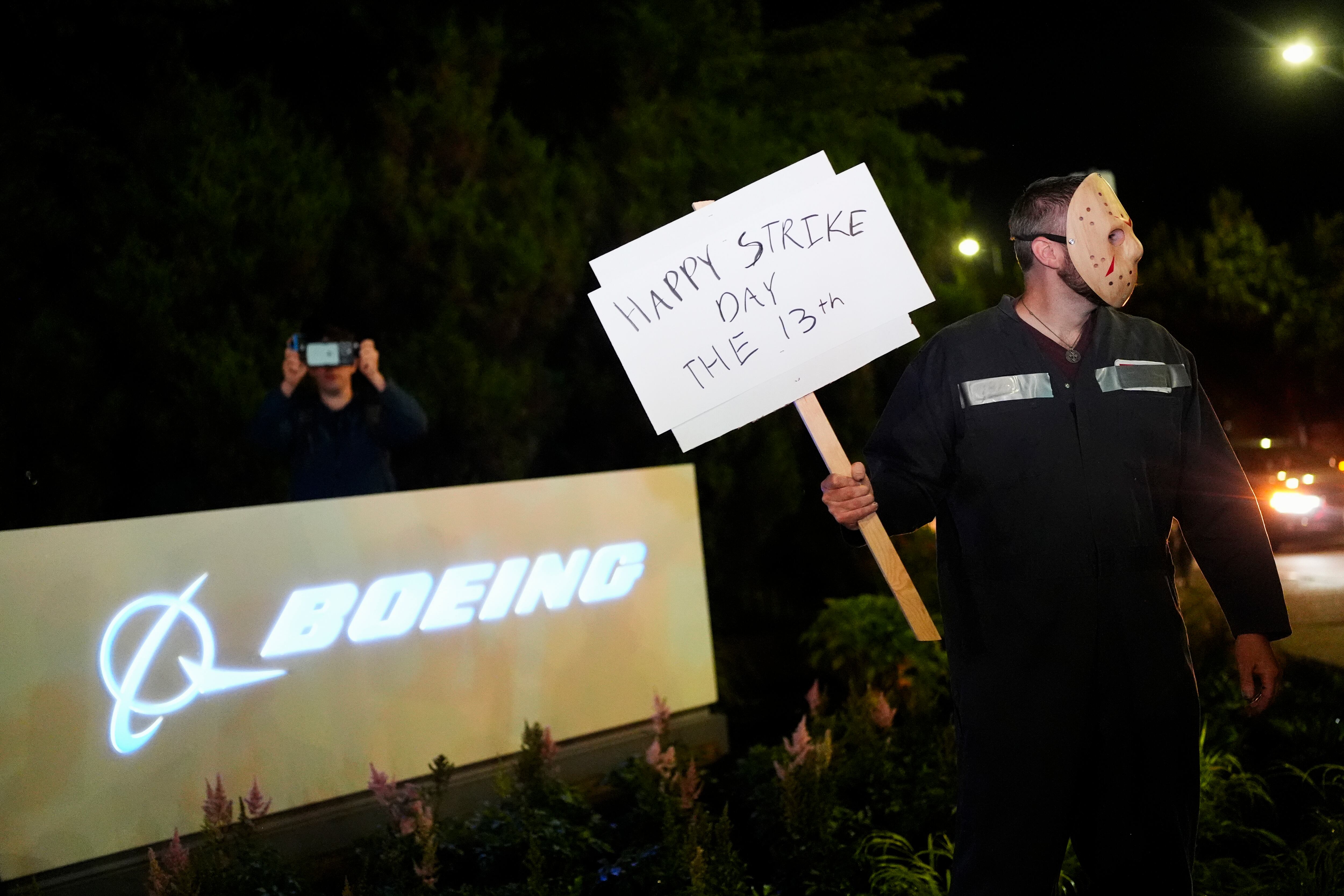 Un trabajador de Boeing usa una máscara mientras sostiene un cartel de "feliz día de la huelga" después de que los miembros del sindicato votaron abrumadoramente para rechazar una oferta de contrato e ir a la huelga el viernes 13 de septiembre de 2024, afuera de la fábrica de la compañía en Renton, Washington (AP Foto/ Lindsey Wasson)