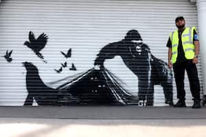 A security guard stands by an artwork by street artist Banksy, the ninth to released in nine days, depicting a gorilla releasing animals, on the front of a shutter outside London zoo, on August 13, 2024. The artist confirmed the work to be theirs after posting an image of it on the social media app Instagram. (Photo by Adrian DENNIS / AFP) / RESTRICTED TO EDITORIAL USE - MANDATORY MENTION OF THE ARTIST UPON PUBLICATION - TO ILLUSTRATE THE EVENT AS SPECIFIED IN THE CAPTION