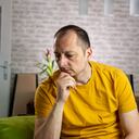 Unhappy depressed caucasian male sitting and lying in living room couch feeling desperate a lonely suffering from depression. Unpleasant pain.