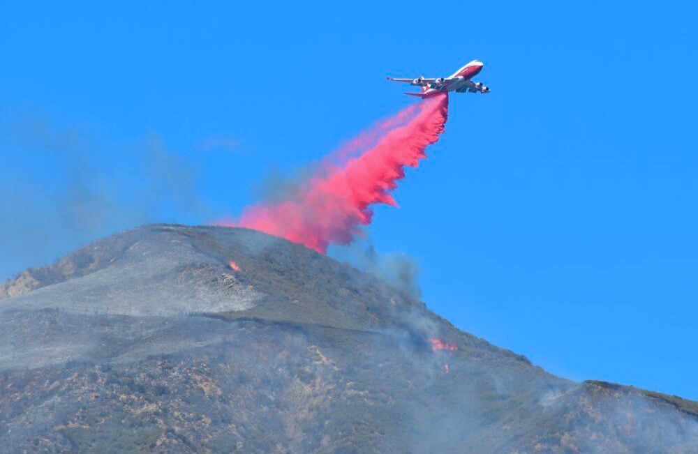 Un avión cae retardante sobre ascuas ardientes y pequeños incendios en la cima de una montaña en Fillmore. Los implacables vientos avivaron enormes llamas en el sur de California, donde cientos de miles de personas se han visto obligadas a huir de múltiples incendios devastadores en el área de Los Ángeles y nuevos brotes cerca de San Diego. FREDERIC J. BROWN / AFP