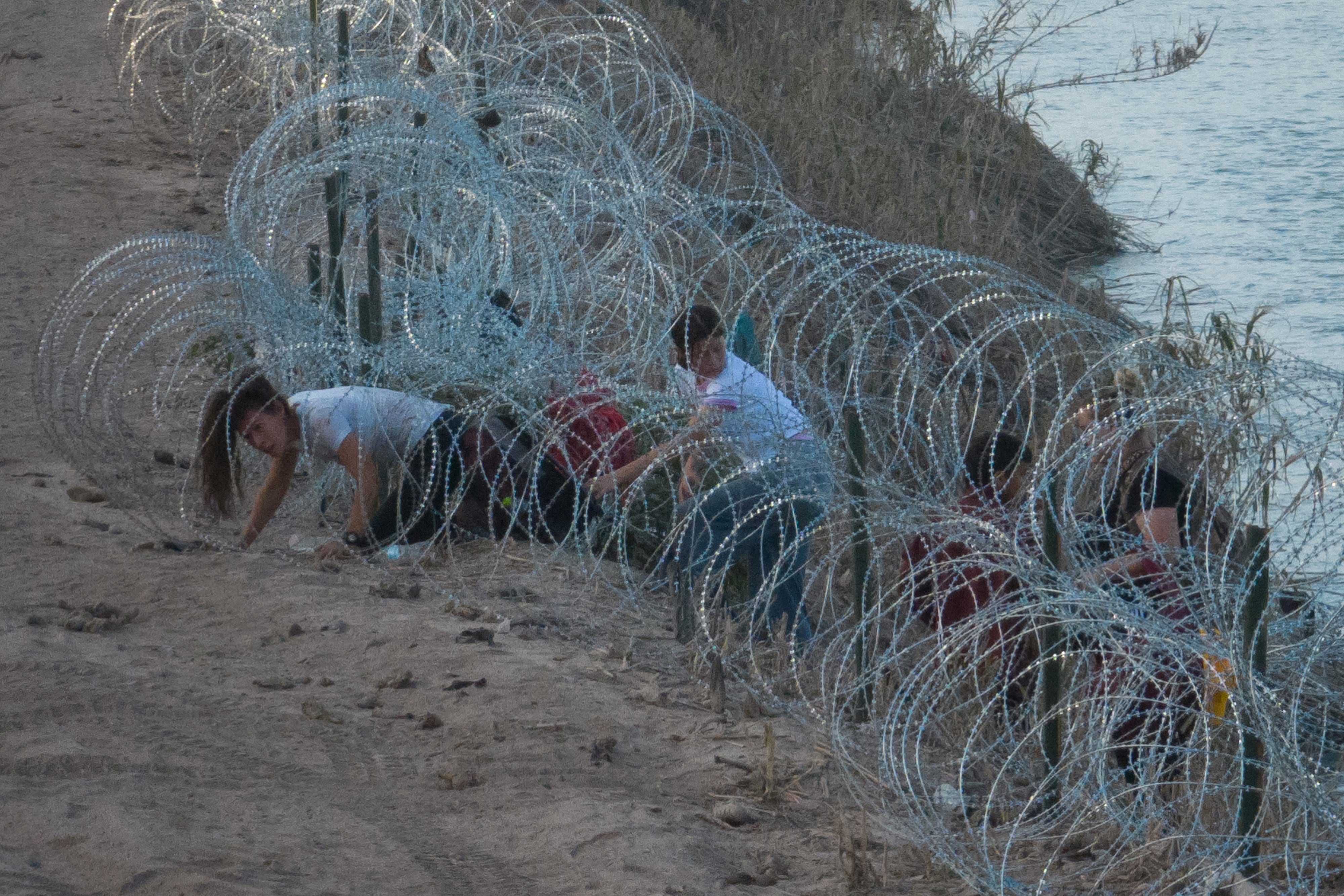 Una mujer de Colombia se arrastra a través de un alambre de concertina, desplegado para disuadir a los migrantes, mientras conduce a sus hijos a través del río Grande hacia Eagle Pass, Texas, EE. UU., 27 de julio de 2023. REUTERS/Adrees Latif