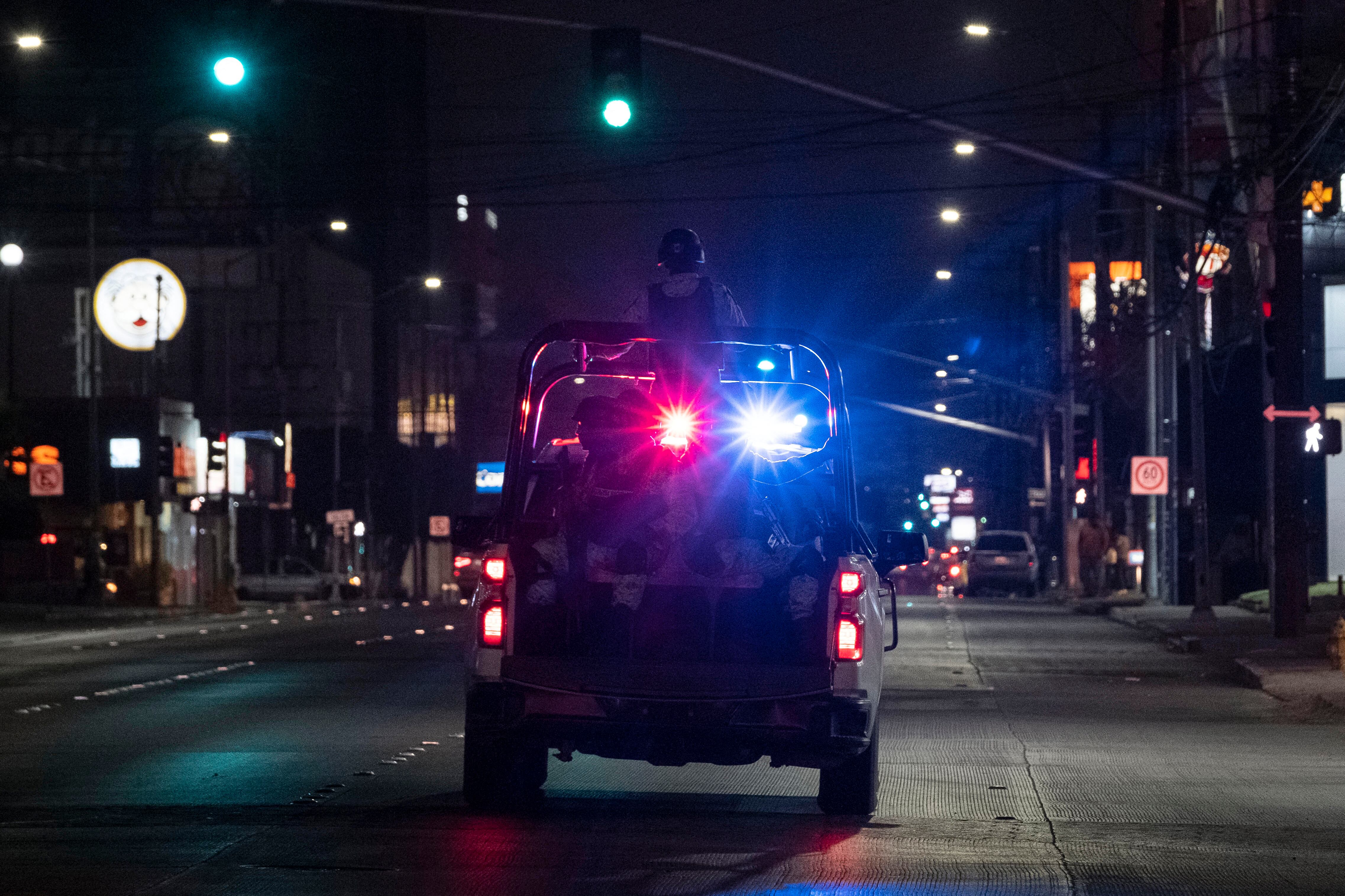 Miembros armados de la Guardia Nacional pasan por delante del lugar donde se encuentra un vehículo de transporte quemado tras ser incendiado por individuos no identificados en Tijuana, estado de Baja California, México, el 12 de agosto de 2022. (Photo by Guillermo Arias / AFP).