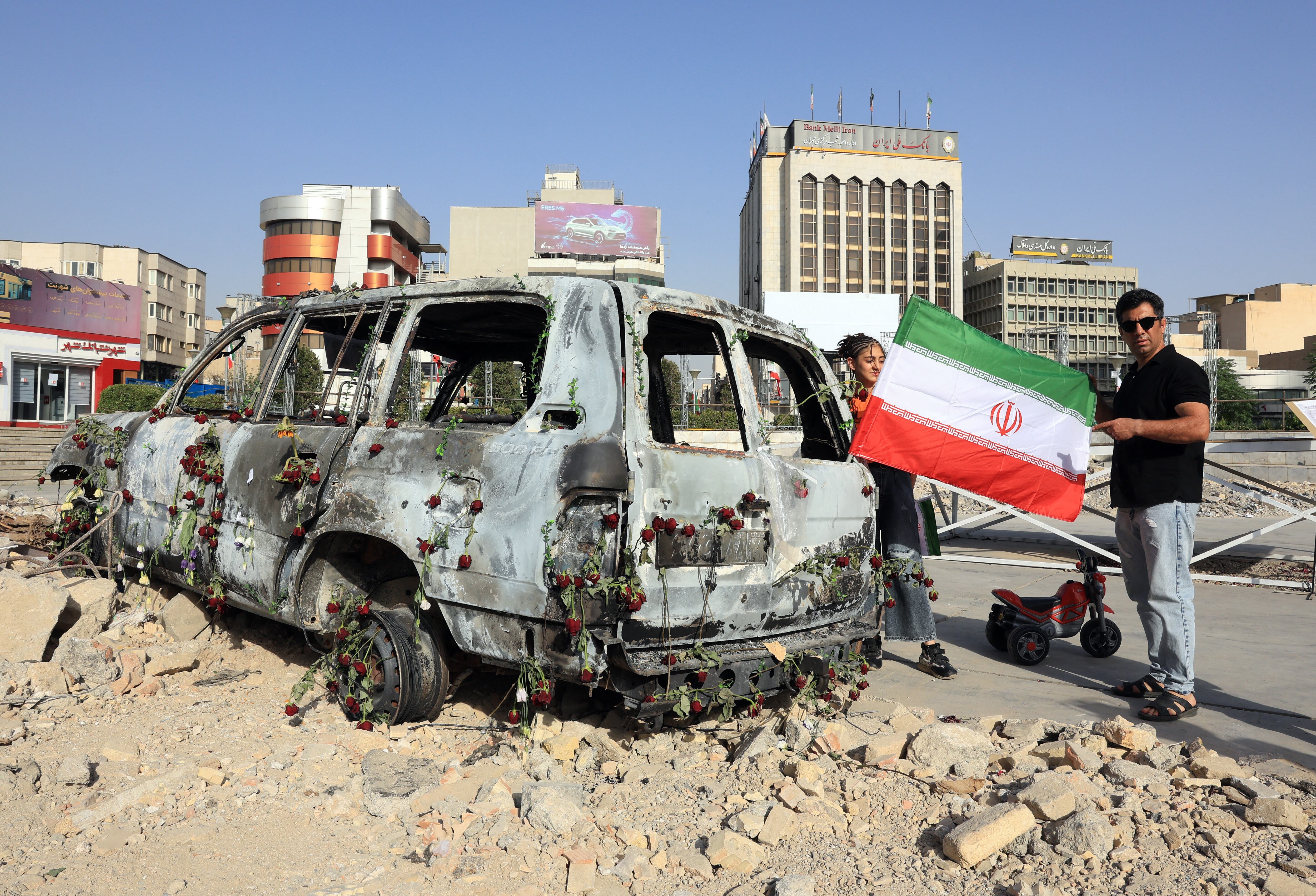 A man holds an Iranian flag by an Iranian Red Crescent ambulance that was destroyed during an Israeli strike, displayed in Tehran on June 23,2025. Israel struck Tehran and Iran fired missiles on June 23, as the war between the longtime foes raged for its 11th day after the United States sent bombers to attack the Islamic republic's nuclear sites. (Photo by ATTA KENARE / AFP)