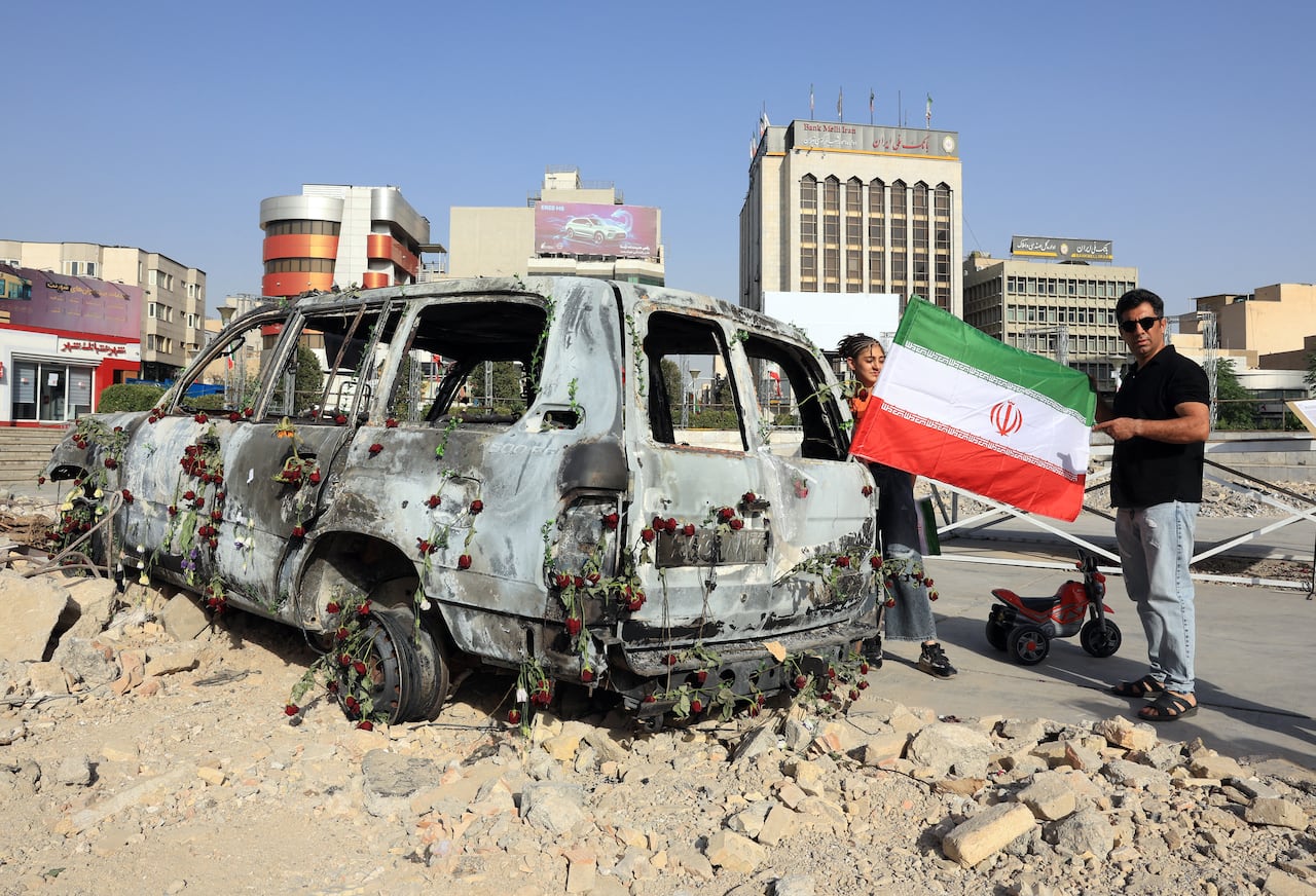 A man holds an Iranian flag by an Iranian Red Crescent ambulance that was destroyed during an Israeli strike, displayed in Tehran on June 23,2025. Israel struck Tehran and Iran fired missiles on June 23, as the war between the longtime foes raged for its 11th day after the United States sent bombers to attack the Islamic republic's nuclear sites. (Photo by ATTA KENARE / AFP)