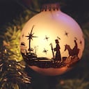 Adorno navideño con silueta de belén con María, José y Belén. El adorno cuelga de la rama del árbol